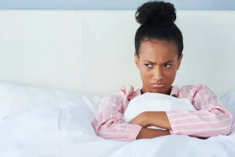 Chica enfadada en la cama, pensando en excusas para no quedar.